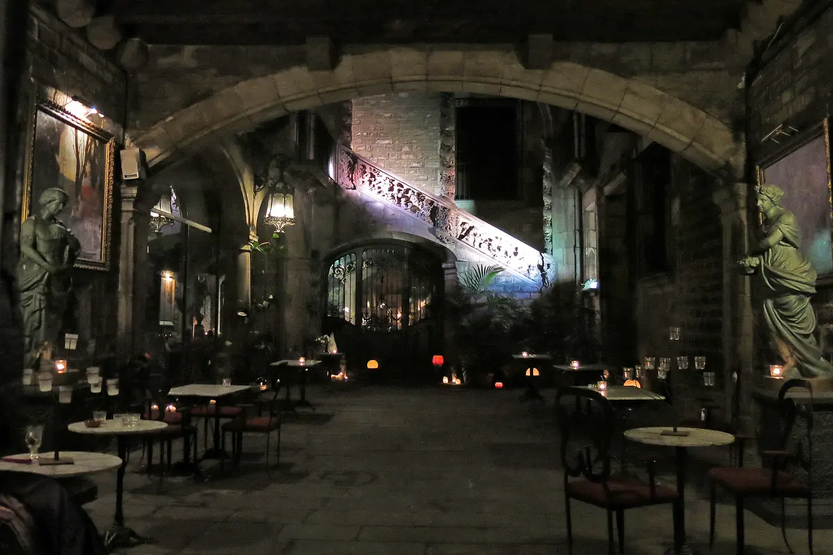 The courtyard of Palau Dalmases at night, with candlelit tables under stone arches and statues on either side